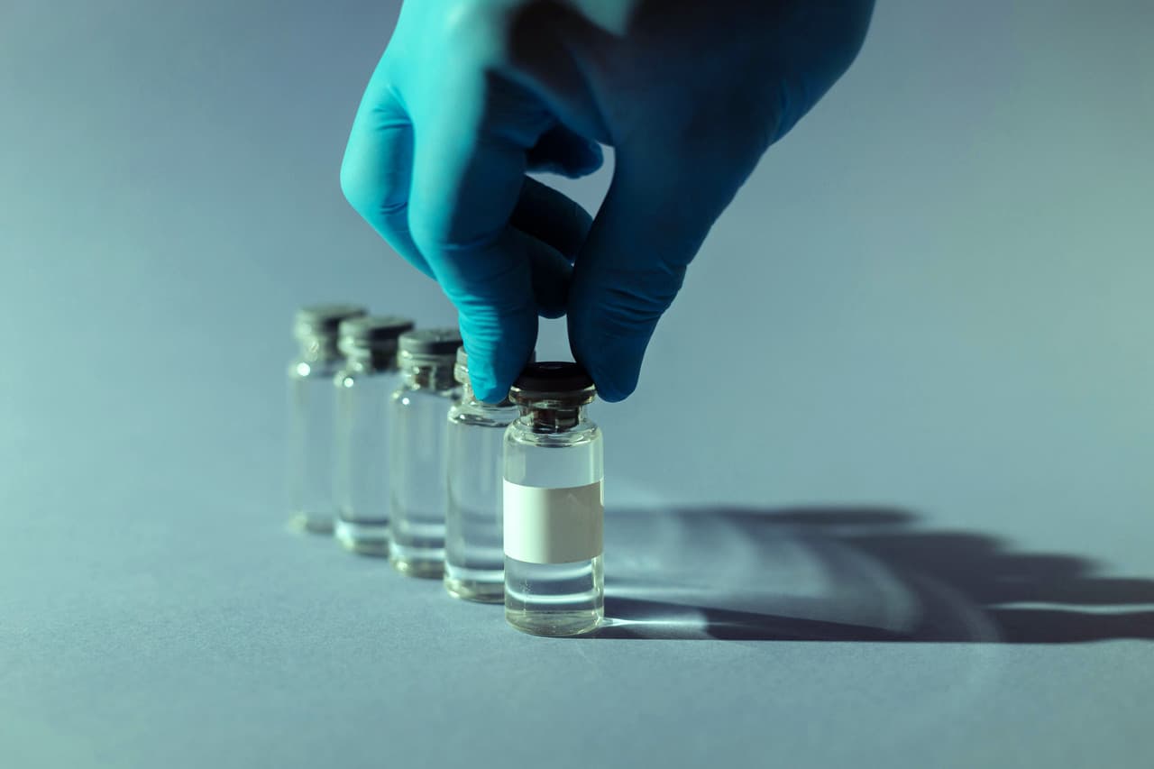 Gloved hand selecting a clear medication vial from a row of vials